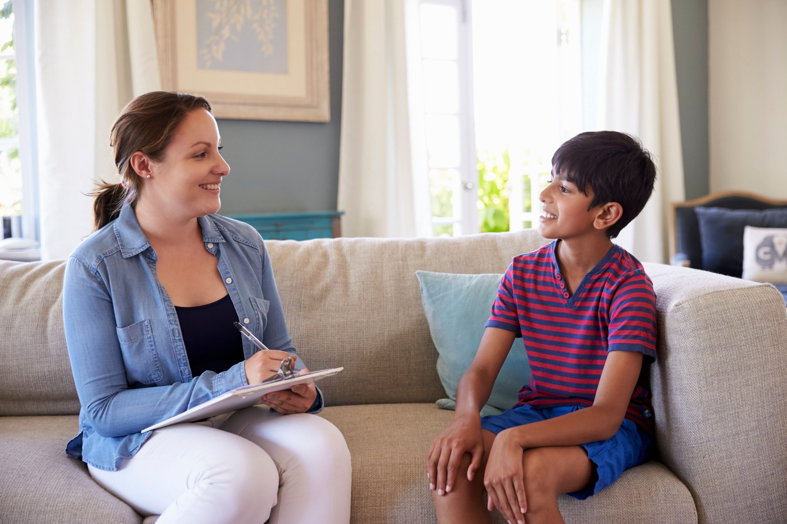 Woman with a clipboard talking to a young boy in a living room 